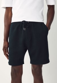 Black patterned shorts with a textured design, featuring an elastic waistband and adjustable drawstrings. Pockets are visible on the sides.