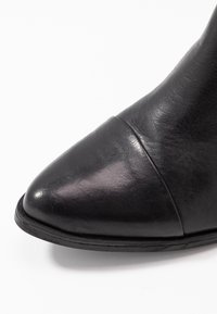Stivale alla caviglia in pelle nera con punta affusolata, dettagli delle cuciture e finitura liscia. La suola è nera con una leggera curvatura.