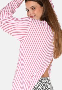 Striped long-sleeve top in white and red with a relaxed fit, featuring a split back that reveals skin. The model wears patterned jeans.