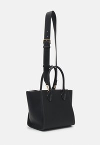 Svart texturerad läderhandväska med dubbla handtag och justerbar axelrem, guldfärgade detaljer och vita stygn.