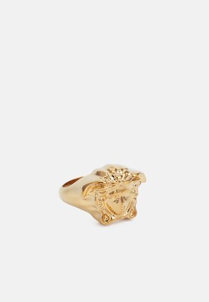 Gouden ring met een reliëfontwerp van een gezicht met vloeiende haren, een glad oppervlak en een iets afgeronde band voor comfort.