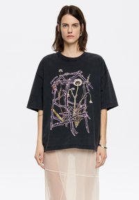 Juodas per didelis t-shirt su gėli�ų grafika purpurine ir kremine spalvomis, su apvaliu kaklu ir trumpomis rankovėmis. Dizaino elemente įtraukta tekstas.