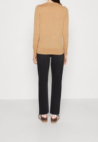 Beige gebreide trui met lange mouwen, gecombineerd met zwarte broek en schoenen met een roze ontwerp en bruine accenten. Soepele textuur, casual pasvorm.