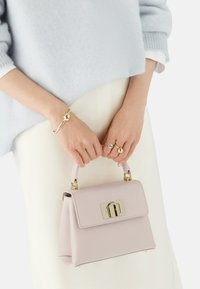 Borsa a tracolla in pelle rosa chiaro con design strutturato, chiusura in hardware dorato e manico corto. Indossata con un maglione azzurro chiaro e una gonna bianca.