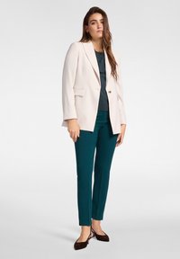Helles pinker Blazer mit Reverskragen, türkisfarbenen Hosen und braunen Ballerinas. Das Outfit hat einen leichten Glanz und eine strukturierte Passform.