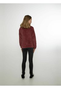Maglione in pile bordeaux con una texture morbida, collo rotondo e maniche lunghe, abbinato a jeans skinny neri e sneakers nere.