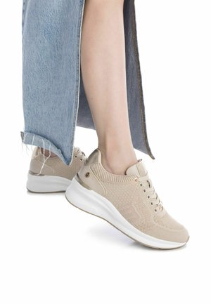Zapatillas de punto beige con una suela blanca elegante, que presentan patrones texturizados y acentos dorados. Llevadas junto a una falda de mezclilla azul clara.