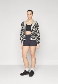 Zebra-patterned black and cream jacket with a hood, worn over a black crop top and black shorts, paired with black sneakers and white socks.