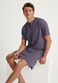 Short-sleeve shirt featuring a geometric pattern in navy, red, and white. It has a buttoned neckline and a loose, relaxed fit.