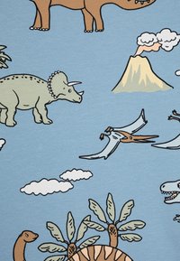 Kokvilnas audums ir ar gaiši zilu fonu, uz kura attēloti karikatūru stila dinozauri, mākoņi, palmu koki un vulkāns zaļā, brūnā un baltā krāsā.