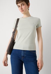 Ljusgrön bomullströja med kort ärm, försedd med en liten logotyp på bröstet. I kombination med mörkblå denimjeans och en brun axelväska.