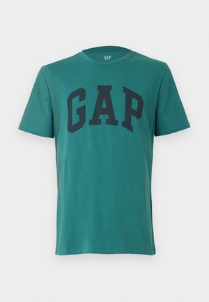 Turquoise T-shirt met korte mouwen en groot zwart "GAP"-logo in het midden van de borst, ronde halslijn en effen achtergrond.