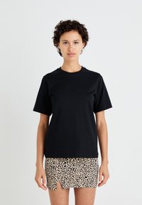 Svart bomulls T-skjorte med korte ermer og rund hals; kombinert med en beige leopardmønstret mini-skjørt med en frontsplitt.