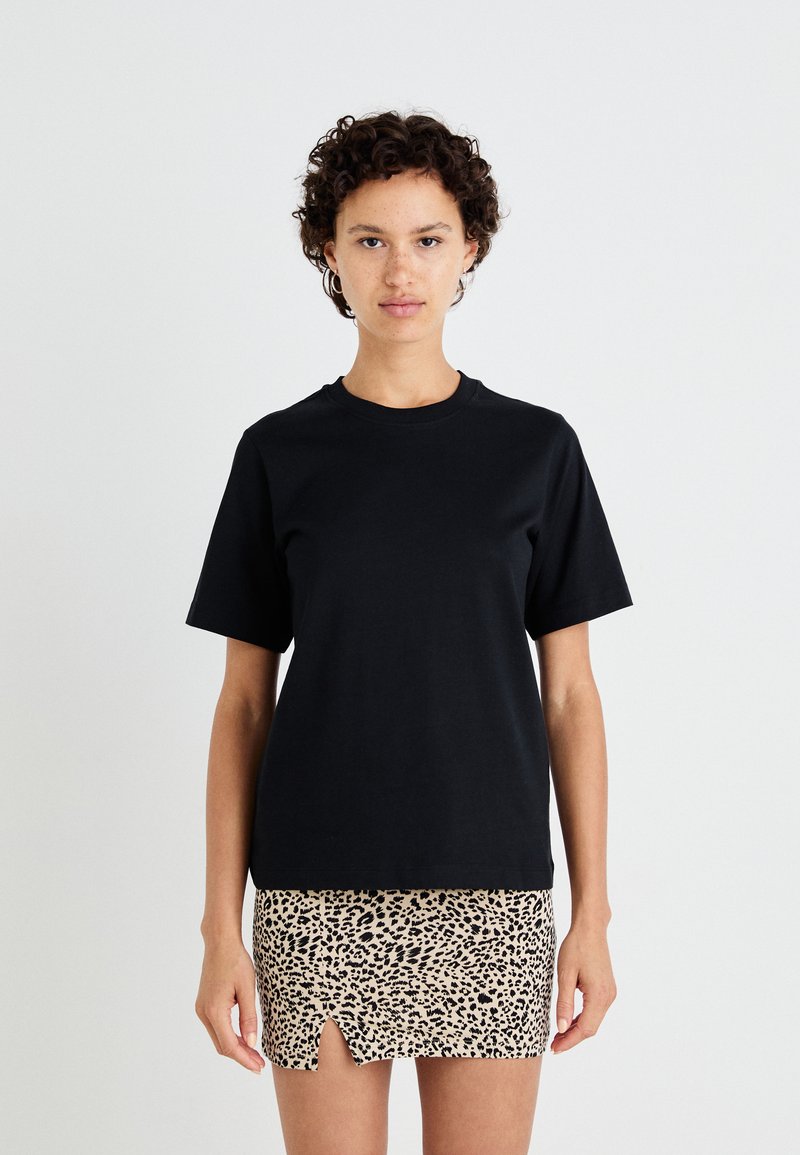 Svart bomulls T-skjorte med korte ermer og rund hals; kombinert med en beige leopardmønstret mini-skjørt med en frontsplitt.
