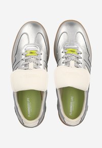 Baskets argentées au fini lisse, avec une sangle élastique blanche, des accents gris et une semelle intérieure verte. Semelle extérieure en caoutchouc à crampons.