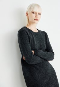 Vestido de malha cinza escuro com mangas longas, decote arredondado e uma textura suave, apresentando uma silhueta ajustada.