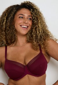 Reggiseno borgogna realizzato in materiale liscio con accenti in rete e un design della coppa strutturato. Spalline regolabili e un motivo testurizzato sul tessuto.