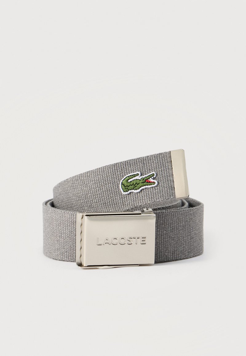Ceinture en tissu gris avec boucle argentée embossée du nom « LACOSTE » et logo crocodile vert brodé à l’extrémité de la lanière.