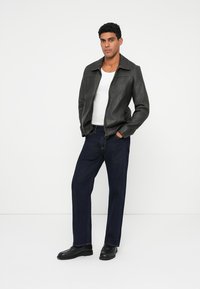 Chaqueta de cuero negra con una textura suave, cierre de cremallera y cuello, combinada con pantalones vaqueros oscuros y zapatos negros.