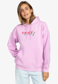 Svetlo ružová mikina s predným vreckom, kapucňou na šnúrku a farebnou grafikou "ROXY" v retro písmene. Mäkkučký materiál a pohodlný strih.