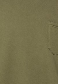 Olivgrön bomullsduk med en slät textur, som har en liten, rektangulär ficka på högra sidan.