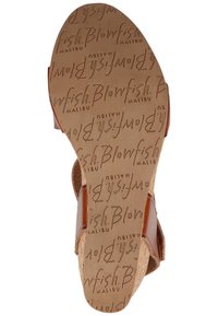 Semelle d’une sandale compensée marron avec un texte embossé répété « Blowfish Malibu » sur la surface inférieure en caoutchouc.