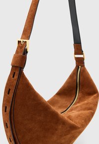 Borsa a spalla in suede marrone con forma curvata, tracolla in pelle nera, accessori in oro e chiusura con zip su un lato.