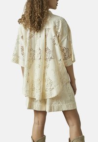 Blonderoverlay skjorte i lys gul med løs pasform, korte ærmer og matchende shorts. Bemærkelsesværdige intrikate blonde mønstre overalt.