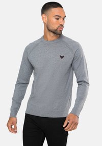 Grå langærmet crewneck sweatshirt med ribbede manchetter og nederkant. Har et lille mørkt logo på brystet, lavet af et blødt stof.
