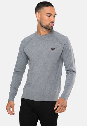 Grå langærmet crewneck sweatshirt med ribbede manchetter og nederkant. Har et lille mørkt logo på brystet, lavet af et blødt stof.