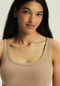 Beżowy prążkowany top na ramiączkach z okrągłym dekoltem, cienkimi ramiączkami i dopasowanym krojem, podkreślający gładką fakturę materiału.