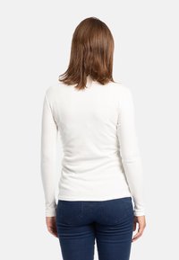 Top bianco a maniche lunghe, aderente, realizzato in tessuto morbido, con scollatura rotonda e superficie liscia, abbinato a jeans blu scuro.