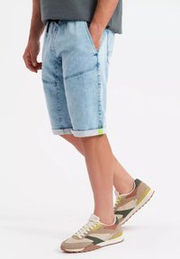 Shorts de mezclilla azul claro con puños enrollados y bolsillos frontales. Combinados con zapatillas en tonos marrón, verde y óxido que presentan cordones blancos y acentos texturizados.