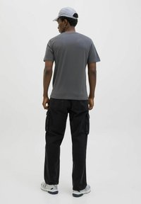Grå t-shirt med korte ærmer parret med sorte cargo-bukser, der har flere lommer. Modellen bærer en lysegrå kasket og grå sneakers.