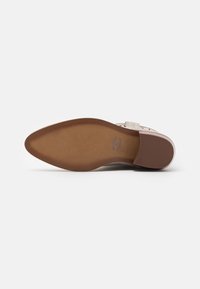 Mule shoe with a beige textured upper, wide strap across the foot, and a brown, slightly curved rubber sole for support.