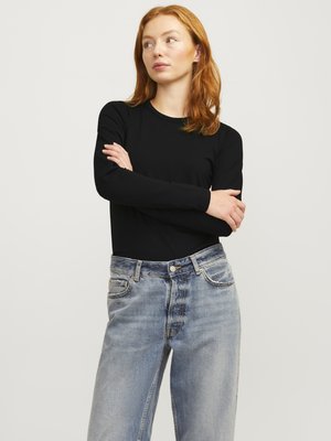 Zwarte lange mouw top met ronde hals, gecombineerd met lichtblauwe, iets versleten wijde jeans. Eenvoudig ontwerp met minimale versieringen.
