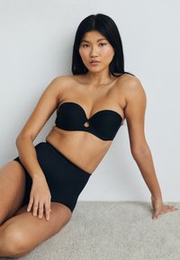 Zwarte strapless bh met een sleutelgatdetail en hoge zwarte onderbroek, beide gemaakt van een gladde stof, weergegeven tegen een neutrale achtergrond.