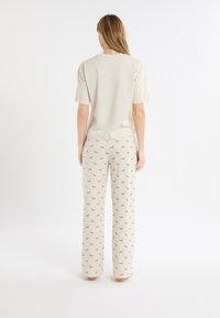 Hellbeiges T-Shirt mit kurzen Ärmeln und lässiger Passform, kombiniert mit cremefarbenen Hosen mit kleinem braunem Hundemuster. Glatte Stofftextur durchgehend.