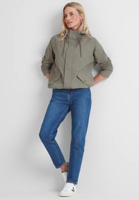 Light olive green cropped jacket with a hood, drawstring closure, dual front pockets, and ribbed cuffs, paired with blue straight-leg jeans and white sneakers.