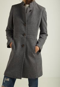 Grå ullblandningsjacka med hög krage, frontknappar, två sidofickor och skräddarsydd passform, med en mjuk textur och klassisk design.