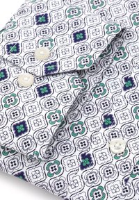 Biała koszula z materiału z kwiatowym wzorem w kolorze granatowym, zielonym i czarnym. Dwa guziki na kołnierzyku o teksturowanym wykończeniu.