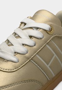 Χρυσό σατέν αθλητικό παπούτσι με λευκά κορδόνια, διαθέτει υφή επιφάνειας και διακριτικές γεωμετρικές λεπτομέρειες. Περιλαμβάνει χρυσή τρύπα κορδονιών.