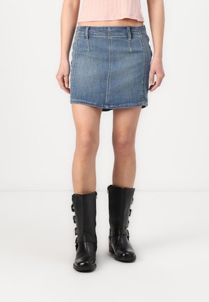 Denim minirok met een aansluitende silhouet, lichtblauwe kleur, voorzakken en stiksels. Gemaakt in combinatie met kniehoog zwarte leren laarzen met gespen.