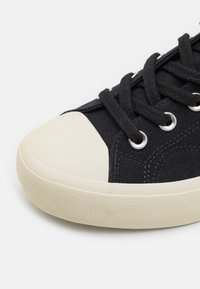 Czarny tenisówka z płótna z białym gumowym czubkiem, teksturowaną podeszwą, metalowymi oczkami i czarnymi sznurowadłami. Prosty design o niskim profilu.