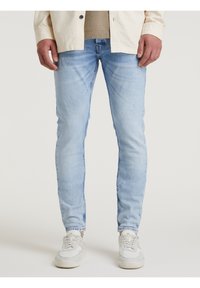 Ljust blå, slim-fit jeans med en urtvättad finish och subtila slitningsdetaljer. Bärs med vita och grå sneakers.