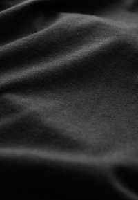 Gros plan d'un tissu noir doux avec des plis subtils et une texture lisse sous un éclairage diffus.