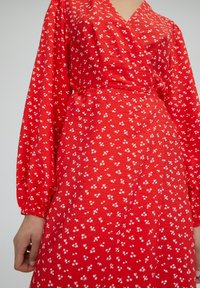 Vestido rojo con un diseño envolvente, que cuenta con mangas largas abullonadas y patrones florales blancos en toda su superficie. Hecho de una tela suave y ligera.