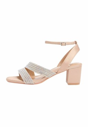 Bézs blokk sarokszandál bokapánttal és két széles, strasszkövekkel díszített keresztpánttal a nyitott lábujjak felett.