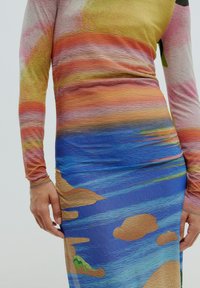 Robe à manches longues présentant un design texturé en dégradé avec des tons terreux en haut, se dégradant vers des motifs vibrants de bleu et de sable en bas.