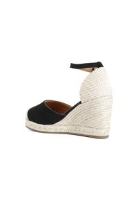 Scarpa wedge nera in suede con tacco in giute intrecciato, cinturino alla caviglia e dettaglio in tessuto a scacchi sul retro. Texture liscia con punta arrotondata.